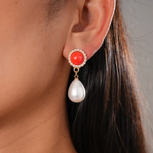 Detail of red stone stud and white drop pearl earring with gold metal on ear
