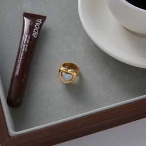 Top view of a gold heart-shaped stainless steel ring with white pearl inlay on a velvet tray