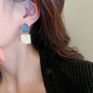Detail of geometric silver needle earrings with blue oval and pearlescent square pendant