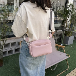 Sac bandoulière rose texture litchi avec large sangle rayée dans un décor de café extérieur