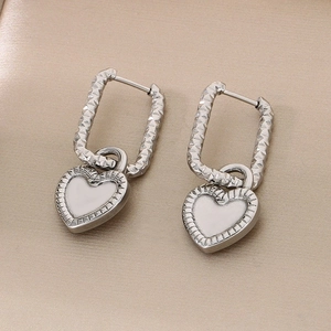 Gros plan de boucles d'oreilles cœur en argent avec émail blanc et créoles texturées