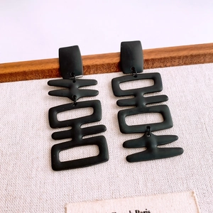 Macro detail of matte black Double Happiness character earrings with tassel on wood