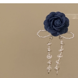 Dettaglio del fermaglio a rosa in denim blu con fiocco di perle e nappa elegante