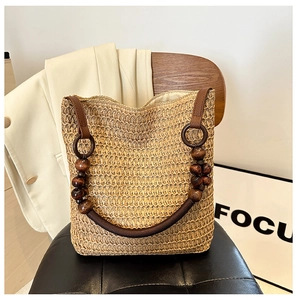 Close-up of woven straw tote bag featuring wooden beads and premium leather straps