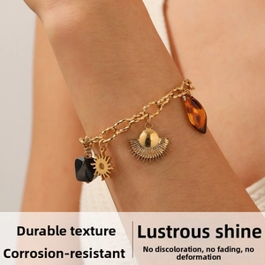 Dettaglio di un bracciale a catena dorata con ciondoli a sole, ventaglio e resina