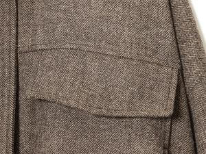 Macro shot of brown herringbone wool jacket showing flap pocket and premium stitching