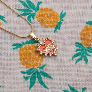 Vue détaillée du pendentif cœur doré avec émail rouge, motif œil et cristaux brillants