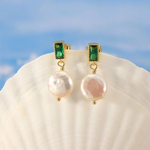 Detailed shot of emerald zircon and natural freshwater pearl earrings on a sea shell