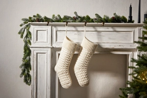 Detailed knit texture of ivory Christmas stockings hanging on a white festive fireplace