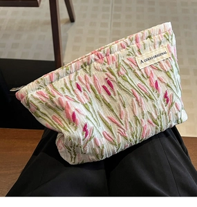 Canvas makeup bag with pink tulip embroidery on model's lap in natural setting