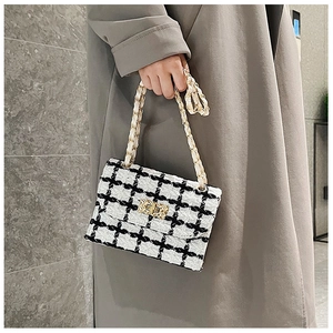 Detail of the black and white plaid tweed shoulder bag with gold chain strap held by a model