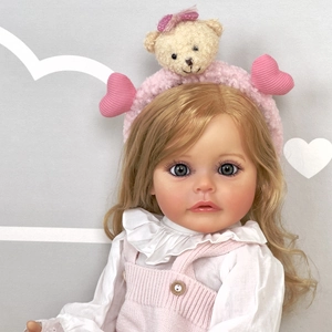 Lifelike 55cm reborn baby doll with blonde curls and pink bear headband in knit overalls