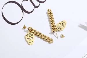 Detailed close-up of gold punk earrings featuring skull charms and Cuban link chains