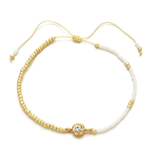 Close-up of golden and white seed bead bracelet with crystal charm and adjustable cord