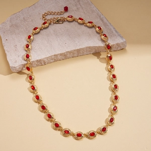 Detailed close-up of a vintage gold oval necklace with red rhinestones on a stone prop