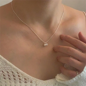Close-up of a delicate silver necklace with pearl and zircon charms on a model collarbone