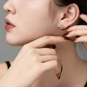 Close-up of a silver bow-shaped stud earring with clear zircon on a model ear