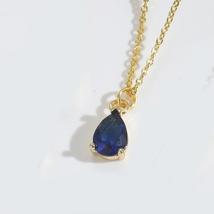 Macro shot of gold necklace with pear-shaped blue waterdrop pendant and claw setting