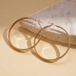 Detailed view of gold textured hoop earrings with marble prop on beige background
