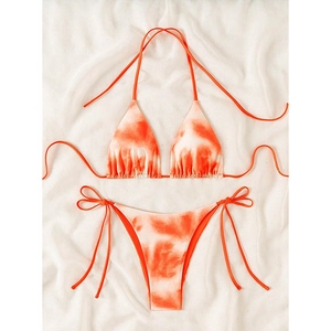 Detailed flat lay of orange and white tie-dye bikini set on a soft textured fabric