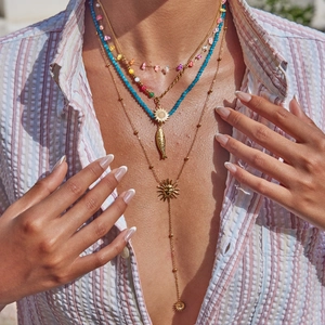 Detail of layered gold necklace with colorful beads and sun charms on a model