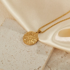 Detail of gold sun pendant necklace with twisted rope chain on textured stone surface
