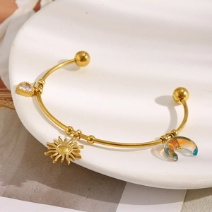 Bracciale rigido bohémien in oro e acciaio con ciondoli sole, luna e cuore su vassoio bianco