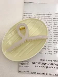Detail of a translucent pink oversized hair claw clip on a ceramic plate with newspaper