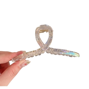 Iridescent transparent resin shark hair claw clip held against a white background