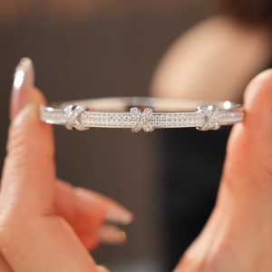Macro shot of silver X-shaped clasp bangle with pavé zirconia stones and polished finish