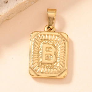 Macro shot of gold square pendant with letter B and radial texture on stone surface
