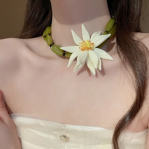 Close-up of white resin flower pendant with green beads and yellow center on necklace