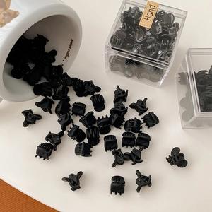 Detailed view of mini matte black hair claws spilling from a cup for hairstyling
