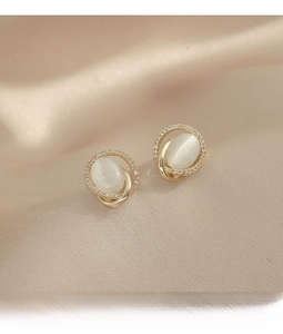 Detailed view of elegant opal gold stud earrings with sparkling zirconia on silk background