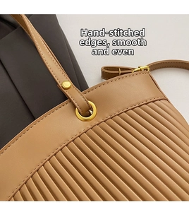 Close-up of khaki leather tote featuring vertical pleated texture and gold metal ring detail