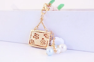 Detailed close-up of golden metal camellia handbag keychain with faux pearl charms