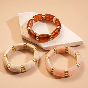 Detail of bamboo-shaped resin bracelets in amber, beige marble, and pink marble patterns