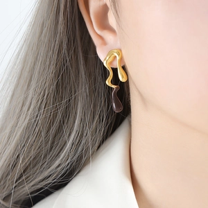 Minimalist gold fluid metal earrings with dark teardrop pendants on model