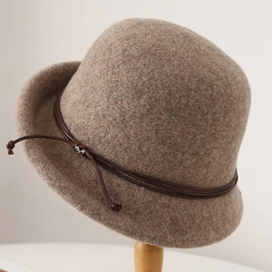 Retro dark brown wool cloche hat with leather string bow on wooden stand