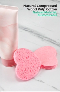 Close-up of heart-shaped pink cellulose sponge on marble surface with skincare tube