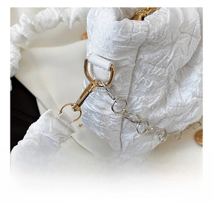 Detailed close-up of golden hardware hooks and pleated texture on white handbag