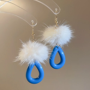 Detailed shot of resin teardrop earrings with fluffy white pom poms and golden hooks