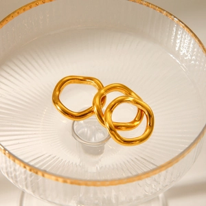 Detailed view of three minimalist gold-plated wave rings inside a clear glass dish
