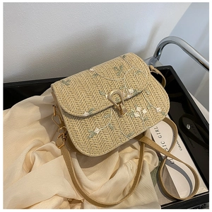 Detailed close-up of beige straw bag with floral embroidery and gold metal lock