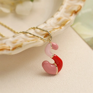 Vue détaillée du pendentif lettre S en émail rose et rouge sur chaîne perlée dorée