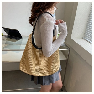 Lifestyle shot of a beige woven tote bag with black shoulder strap for summer beach trips
