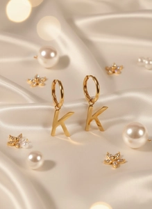 Detailed close-up of golden letter K charm earrings on elegant silk background