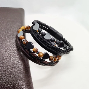 Dettaglio di bracciali multistrato in pelle intrecciata con ciondoli a cuore e chiusura magnetica