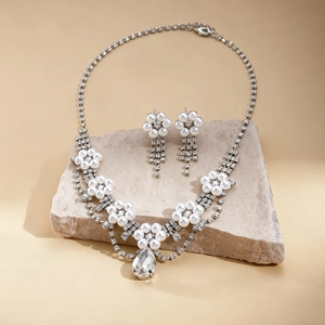 Detail view of crystal flower necklace and teardrop pearl earrings on beige stone