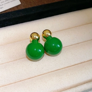 Macro view of green and gold dual-sphere stud earrings on a soft velvet background